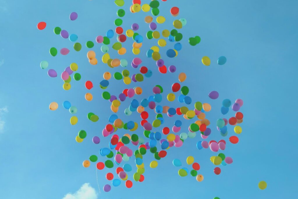 Hundreds of colorful balloons float up into a clear blue sky, creating a vibrant and festive scene.