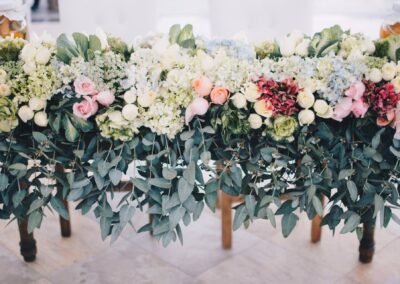 A lush flower arrangement with white, pink, and peach roses, hydrangeas, and greenery drapes over the edge of a table, creating an elegant, garden-inspired centerpiece.