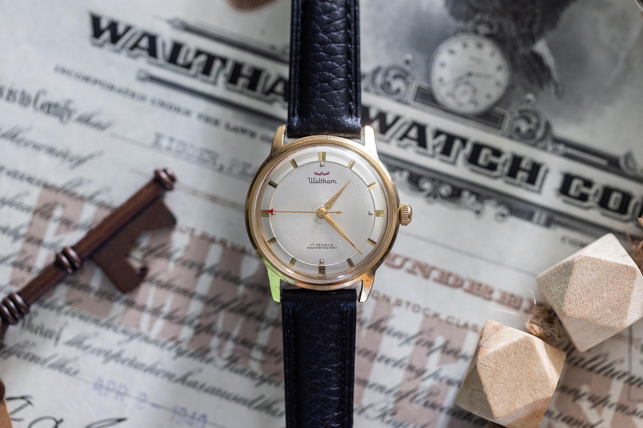 Vintage Waltham 17-jewel wristwatch displayed on an old Waltham Watch Company stock certificate.