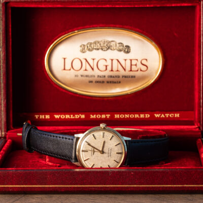 A vintage Longines automatic wristwatch with a black leather strap resting in its red velvet presentation box.