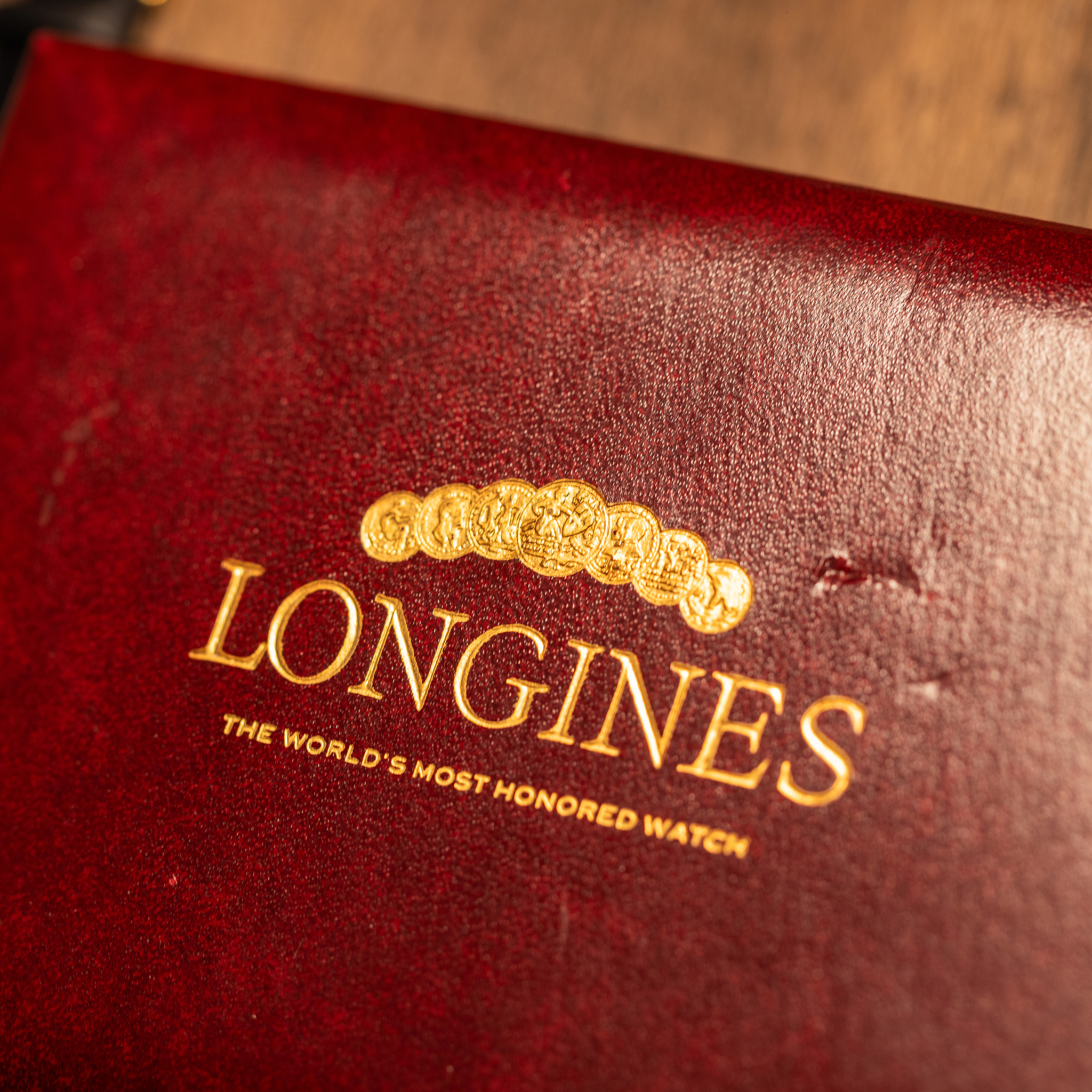 A maroon vintage Longines watch box featuring the gold brand logo, a crest of circular medals, and the text The World’s Most Honored Watch.