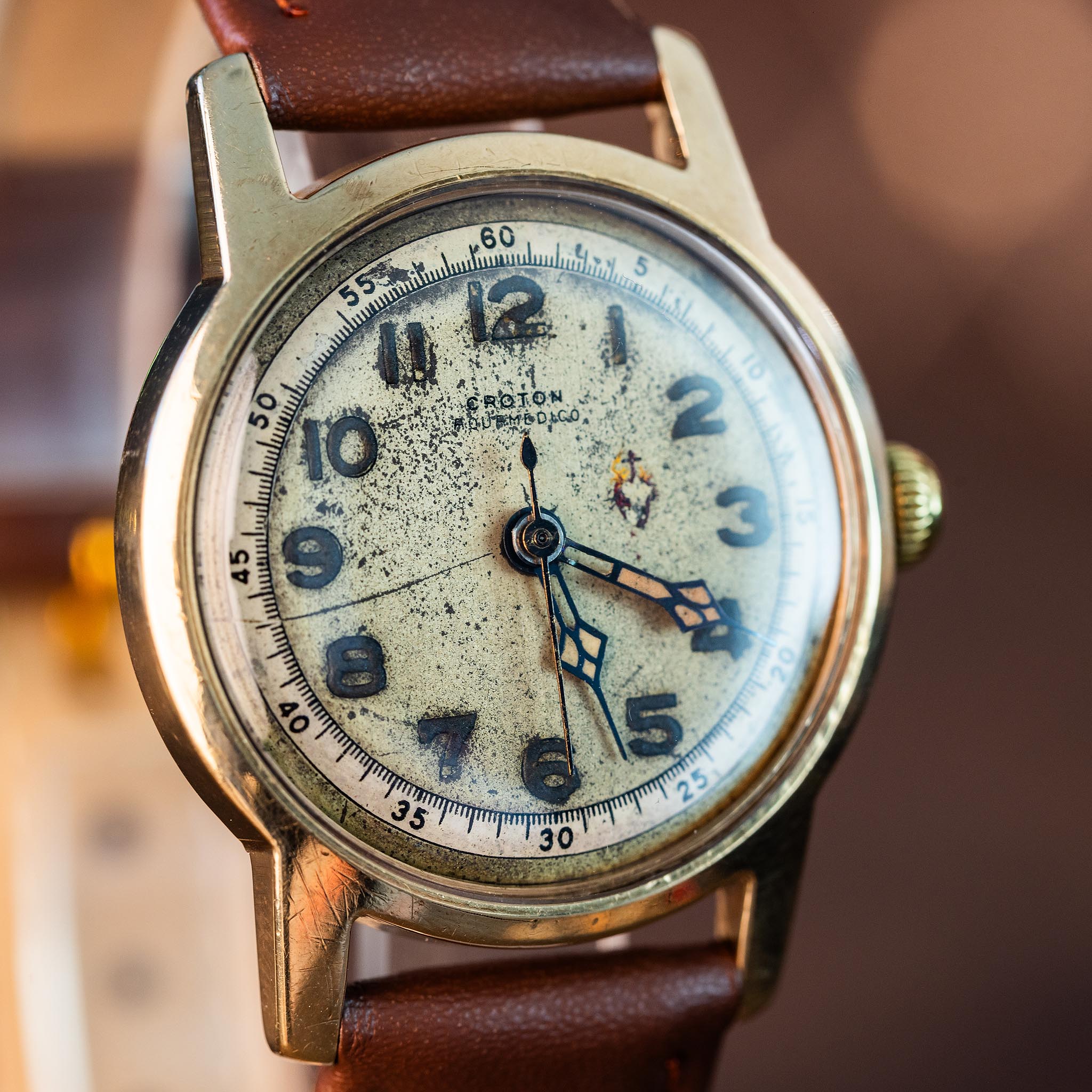 Vintage Croton Aquamedico medical wristwatch with a weathered, textured dial, black Arabic numerals, and a brown leather strap.