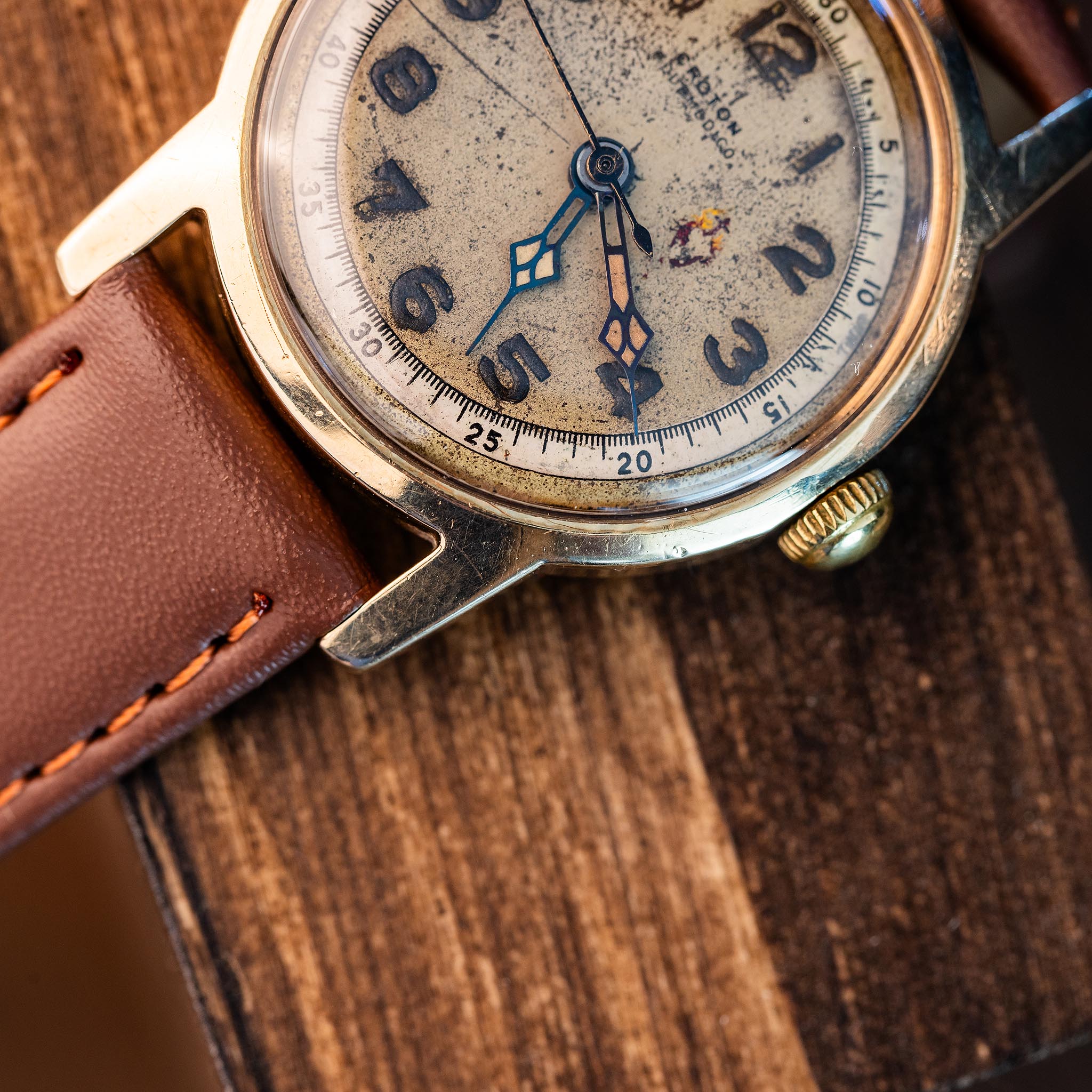 Vintage Croton wristwatch with a weathered, textured 10k gold dial and a brown leather strap on a wooden surface.