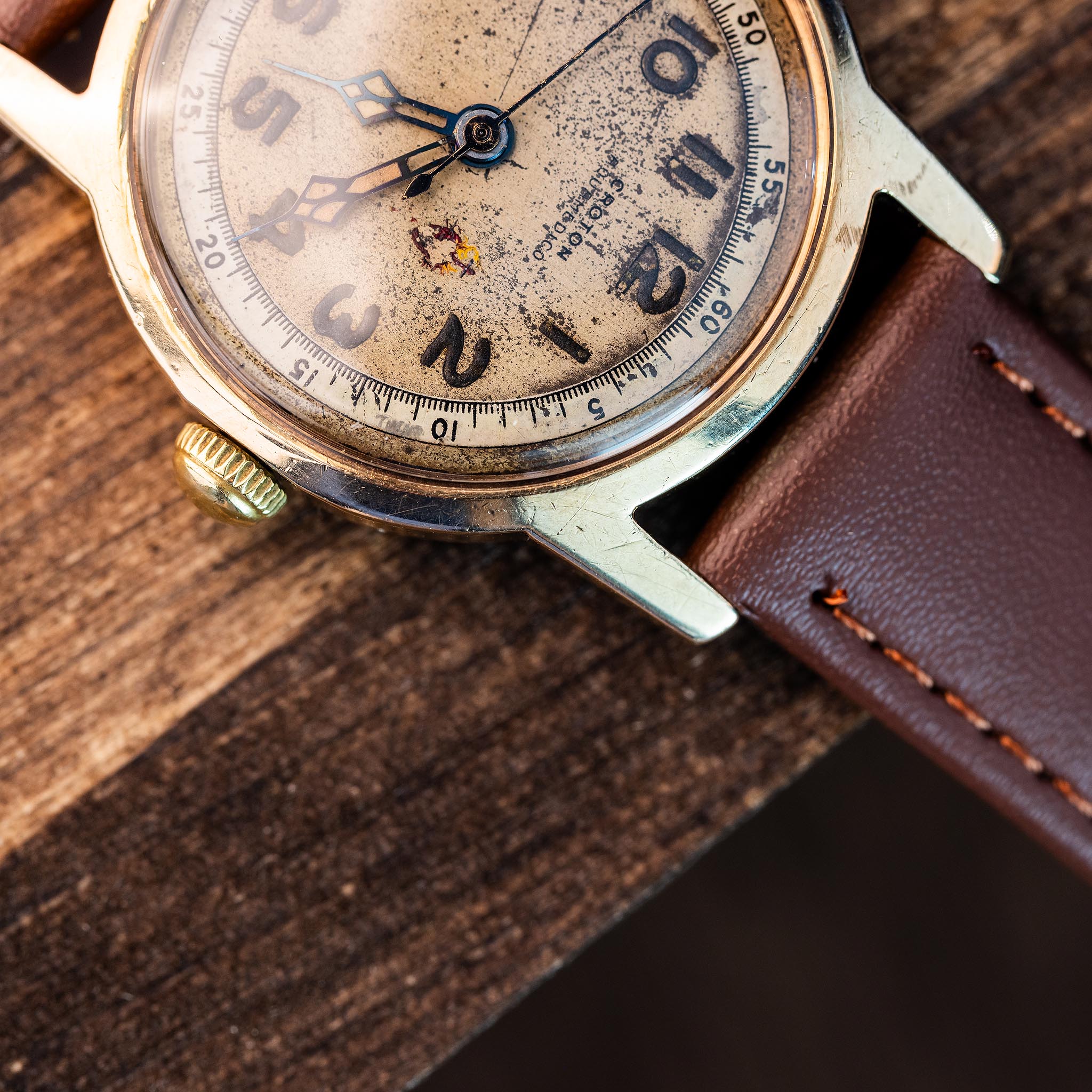 Vintage Croton wristwatch with a weathered, heart-worn face and a brown leather strap resting on a wooden surface.