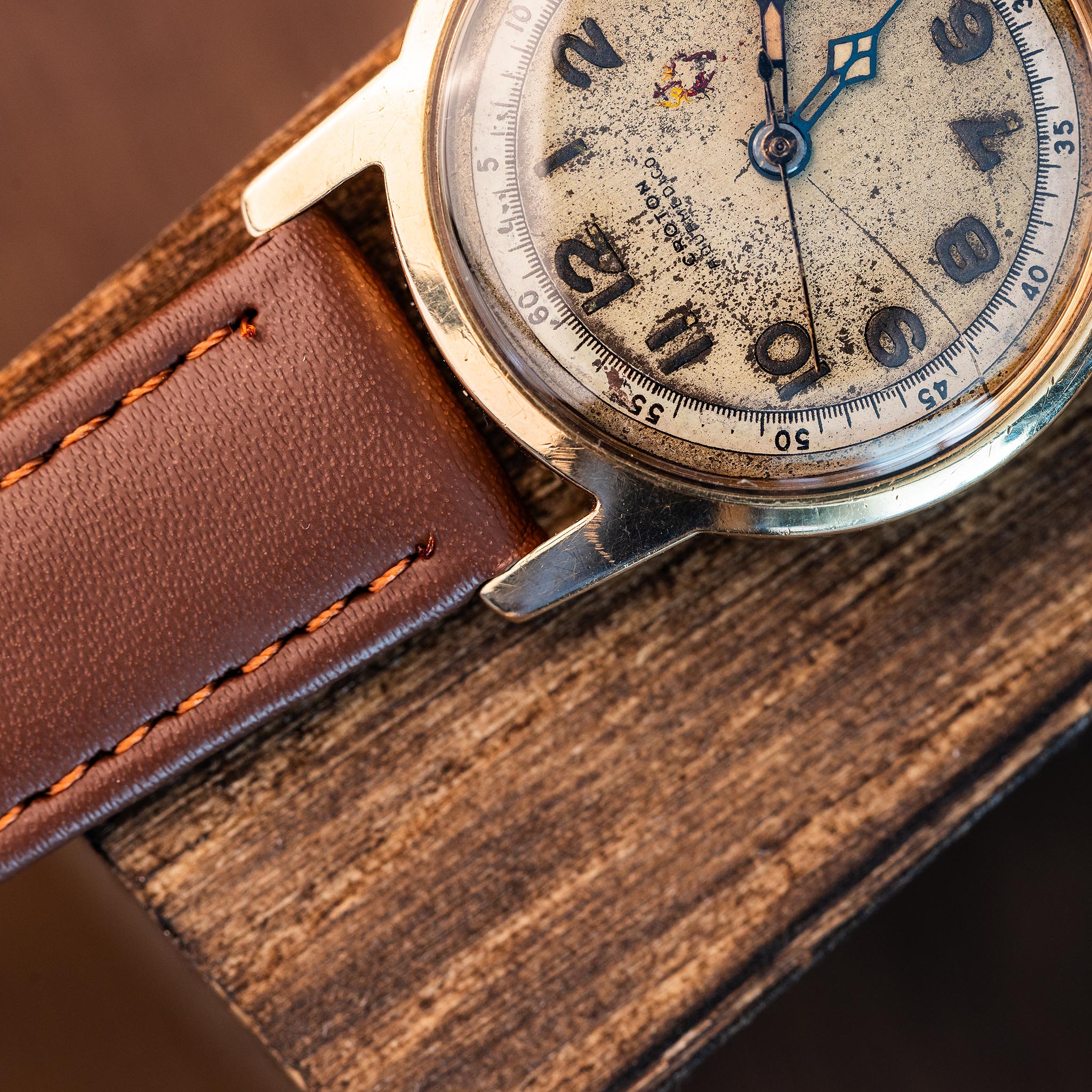 Vintage Croton Aquamedico wristwatch with a weathered, textured dial and a brown leather strap resting on a wooden surface.