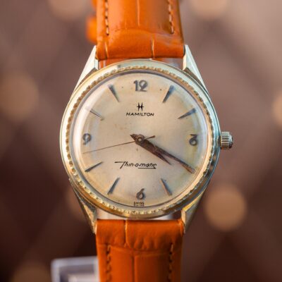 Vintage Hamilton Thin-o-matic wristwatch with a light-colored, found dial, silver markers, and an orange leather strap.