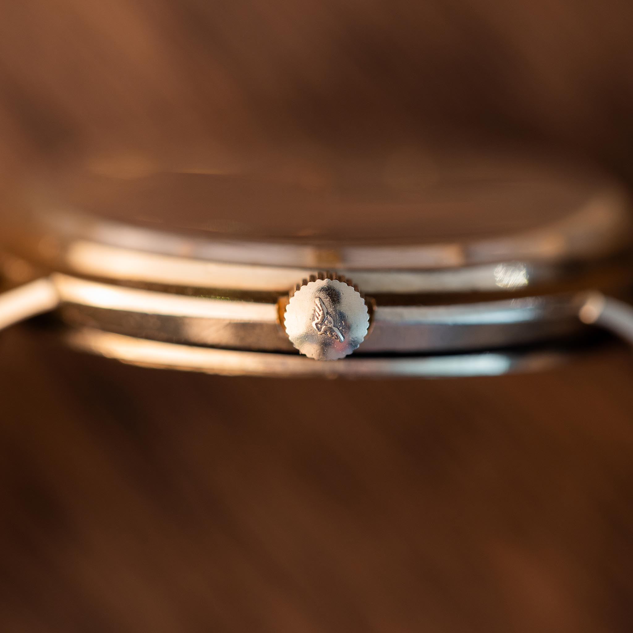 Close-up side view of a vintage Longines watch case featuring a textured crown with an engraved logo.