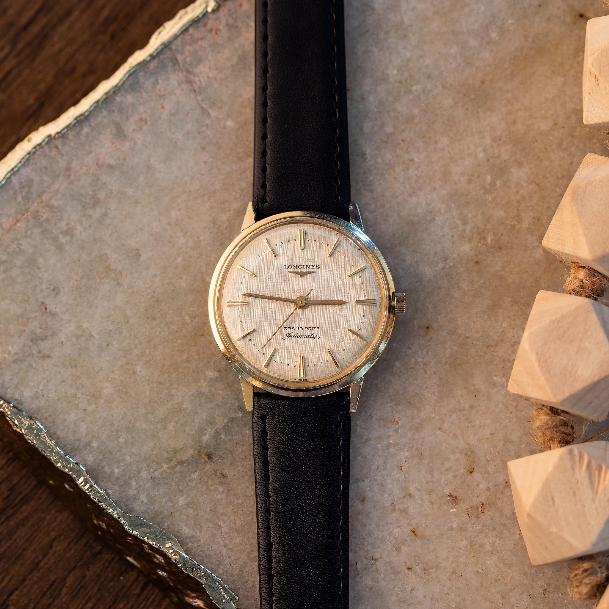 Vintage Longines Grand Prize automatic watch with a 14k gold case, silver dial, and black leather strap.